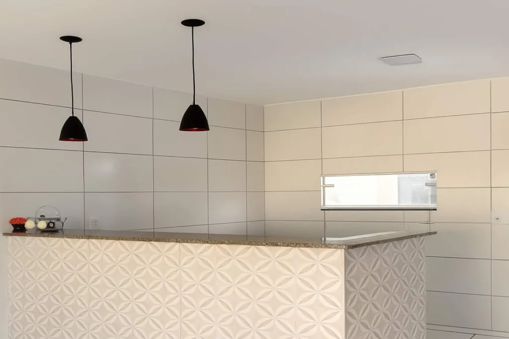 Cozinha da casa em Campo Alegre com bancada em L, revestimento decorativo e luminárias pendentes
