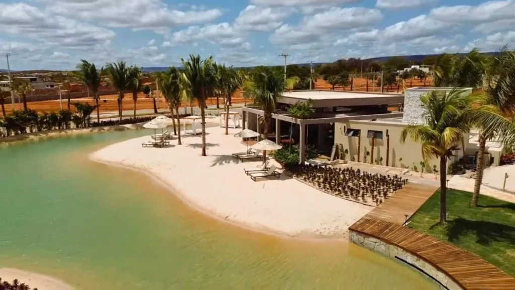 Vista da praia artificial, faixa de areia, palmeiras e espaço de convivência do Conviver Riviera